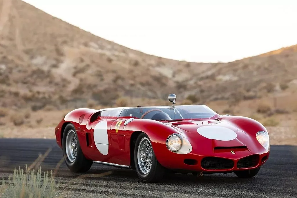 Roter Ferrari-Rennwagen mit weißen Kreisen auf Motorhaube und Türen, geparkt auf Asphaltstraße vor hügeliger Wüstenlandschaft.