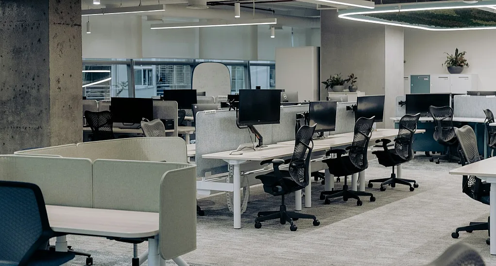 Fotografie eines modernen, offenen Büroumfelds mit mehreren Schreibtischen, ergonomischen Stühlen und Computermonitoren. Helle Beleuchtung, neutrale Farben und Pflanzen schaffen eine produktive und angenehme Arbeitsatmosphäre.