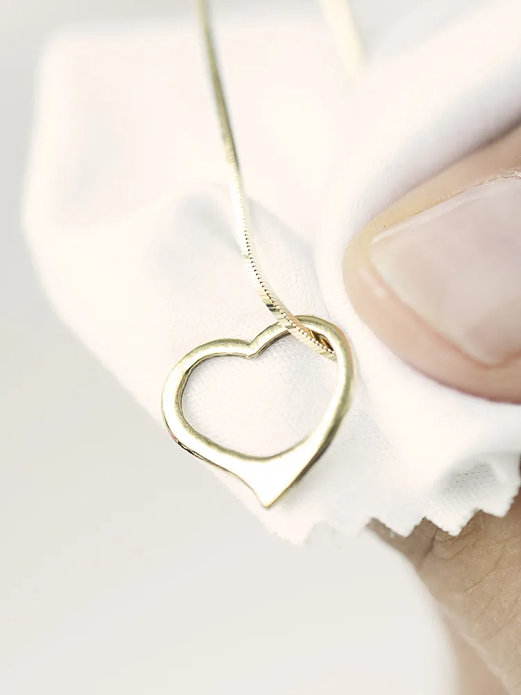 Eine Goldkette mit einem Herzförmigen Anhänger liegt wird von einer Hand auf einem Poliertuch gehalten