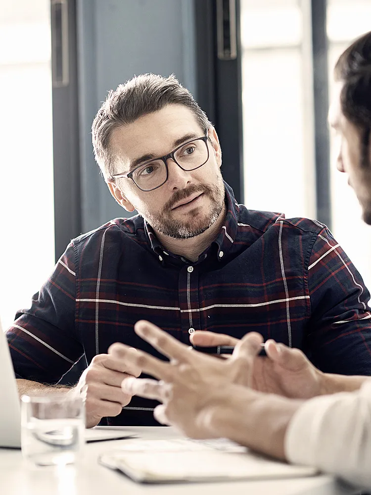 Zwei Männer sitzen an einem Schreibtisch und diskutieren miteinander
