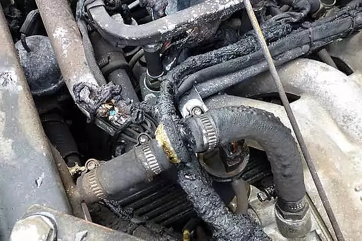 Ein Nahaufnahme des Motorraums mit mehreren Schläuchen und Kabeln. Die Schläuche weisen sichtbare Schäden auf, mit Anzeichen von Verbrennungen oder Schmelzen.