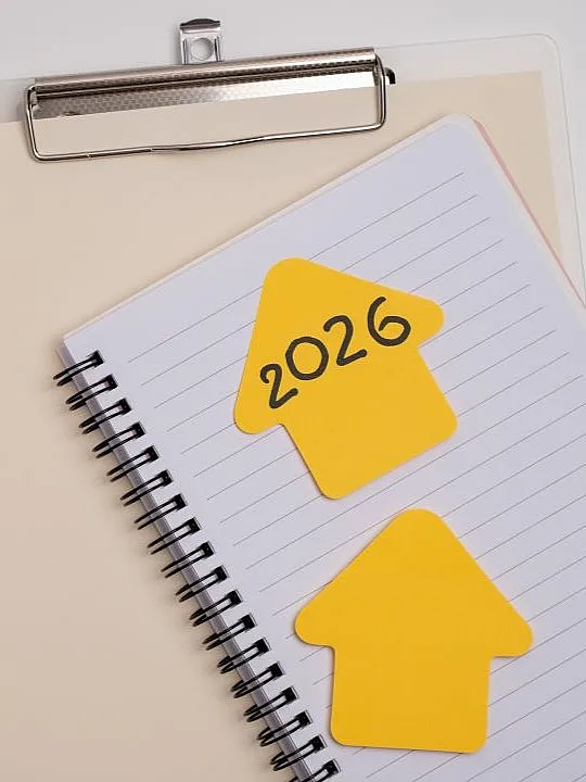 Spiralblock mit zwei gelben, pfeilförmigen Haftnotizen, eine davon mit der Aufschrift „2026“, auf einer linierten Seite. Unter dem Notizbuch befindet sich ein Klemmbrett.