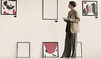 Eine Frau mit Blazer steht vor einer Wand mit Kunstwerken