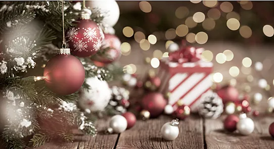 „Festliche Weihnachtsszene mit geschmücktem Baum, roten und weißen Kugeln, Schneeflocken, Zapfen und Lichtern. Im Hintergrund ein gestreiftes Geschenk mit roter Schleife und warme Bokeh-Lichter.