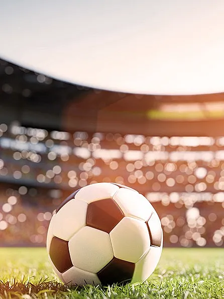 Fußball liegt auf grünem Rasen in einem vollen Fußballstadion mit Zuschauern bei Sonnenschein