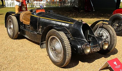 Ein schwarzer Oldtimer-Rennwagen Buggati Type 59 mit Ledersitzen, der im Freien auf Kies ausgestellt ist. Zu den Merkmalen zählen Speichenräder und eine markante, aerodynamische Frontpartie.