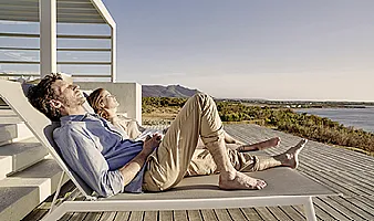 Ein Mann und eine Frau sonnen sich auf Liegen auf einer Terrasse am Meer