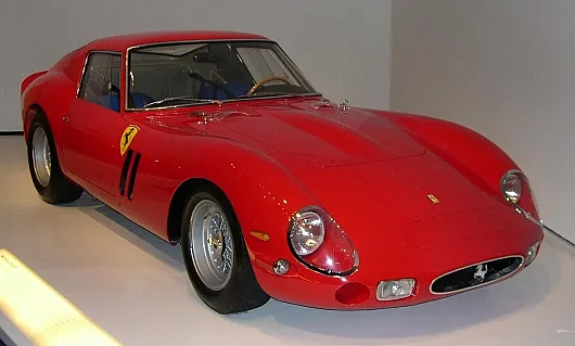 Ein schnittiger, roter Oldtimer-Sportwagen Ferrari 250GTO mit einem fließenden, aerodynamischen Design, markanten Scheinwerfern und einem klassischen Emblem an der Seite, der Geschwindigkeit und Eleganz ausstrahlt.