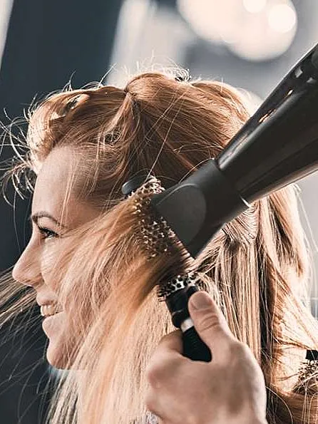 Friseur trocknet das Haar einer lächelnden Frau mit einem Föhn, während er eine Rundbürste benutzt