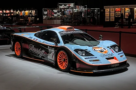 In den Innenräumen ist ein schnittiger Rennwagen McLaren F1 in hellblau-orangefarbenen Tönen ausgestellt. Er besticht durch auffällige Logos und leuchtend orangefarbene Felgen und strahlt eine klassische Rennsportatmosphäre aus.