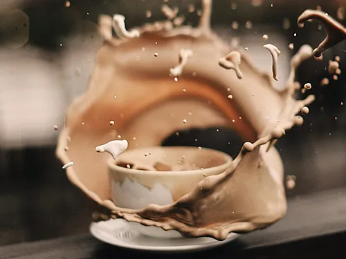 Eine Kaffeetasse die angestoßen wurde. Der Kaffee verspritzt heftig rund um die Tasse