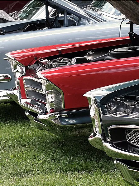 Vier Oldtimer mit offenen Motorhauben parken nebeneinander auf einer grünen Wiese