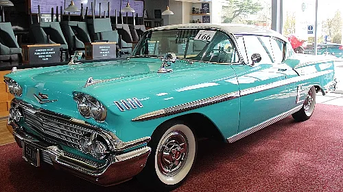 Ein klassischer türkis-weißer Chevrolet Bel Air aus den 1950er oder 1960er Jahren, der auf einem roten Teppich in einem Innenraum ausgestellt ist.