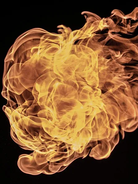 Ein dynamisches und komplexes Flammenmuster vor einem schwarzen Hintergrund. Die Flammen wirbeln und kräuseln sich, wobei sie verschiedene Gelb-, Orange- und Rottöne zeigen.