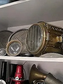Ein Regal mit verschiedenen alten Schiffsleuchten und Laternen aus Messing. Die Leuchten haben unterschiedliche Größen und Formen und sind auf zwei Regalböden verteilt.