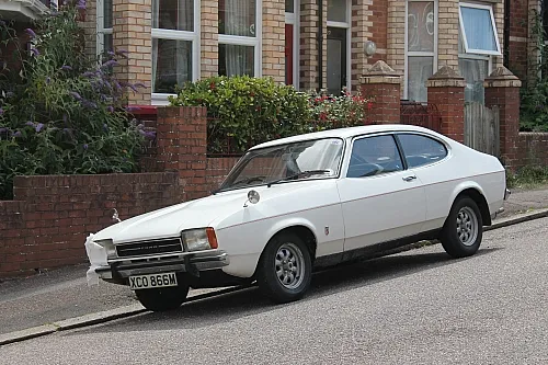 Ford Capri I Oldtimer in Weiß auf einer Straße vor Wohnhäusern, klassisches Sportcoupé mit Kultstatus