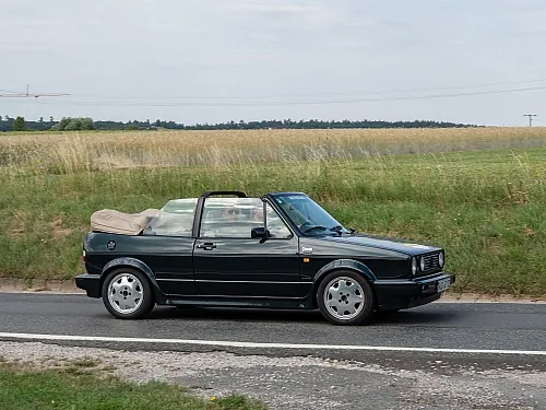 VW Golf Cabrio Oldtimer in Schwarz mit geschlossenem Verdeck auf einer Landstraße in ländlicher Umgebung