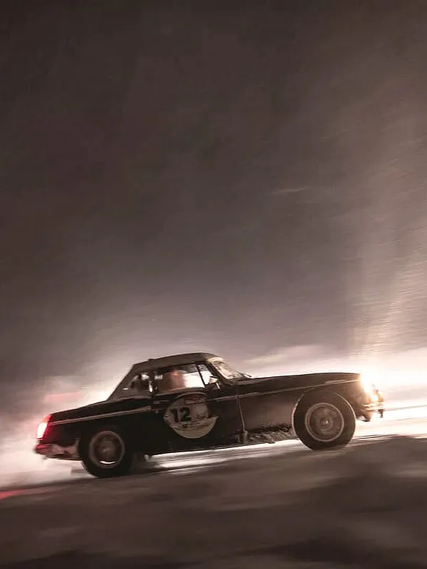 Ein schwarzes Vintage-Sportauto mit der Nummer 12, das mit hoher Geschwindigkeit durch eine verschneite oder vereiste Umgebung fährt.