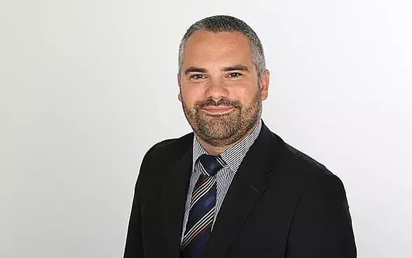 richard weber, der teil des hiscox management team ist, trägt einem dunklen Anzug mit weißem Hemd und blau-schwarz gestreifter Krawatte.