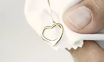 Eine Goldkette mit einem Herzförmigen Anhänger liegt wird von einer Hand auf einem Poliertuch gehalten
