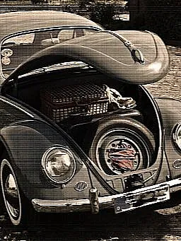 Ein klassischer VW Käfer mit geöffneter vorderer Haube, die einen Ersatzreifen, ein rotes Tuch und einen Picknickkorb im Kofferraum zeigt. Das Auto steht auf einem gepflasterten Weg, umgeben von Blumen.
