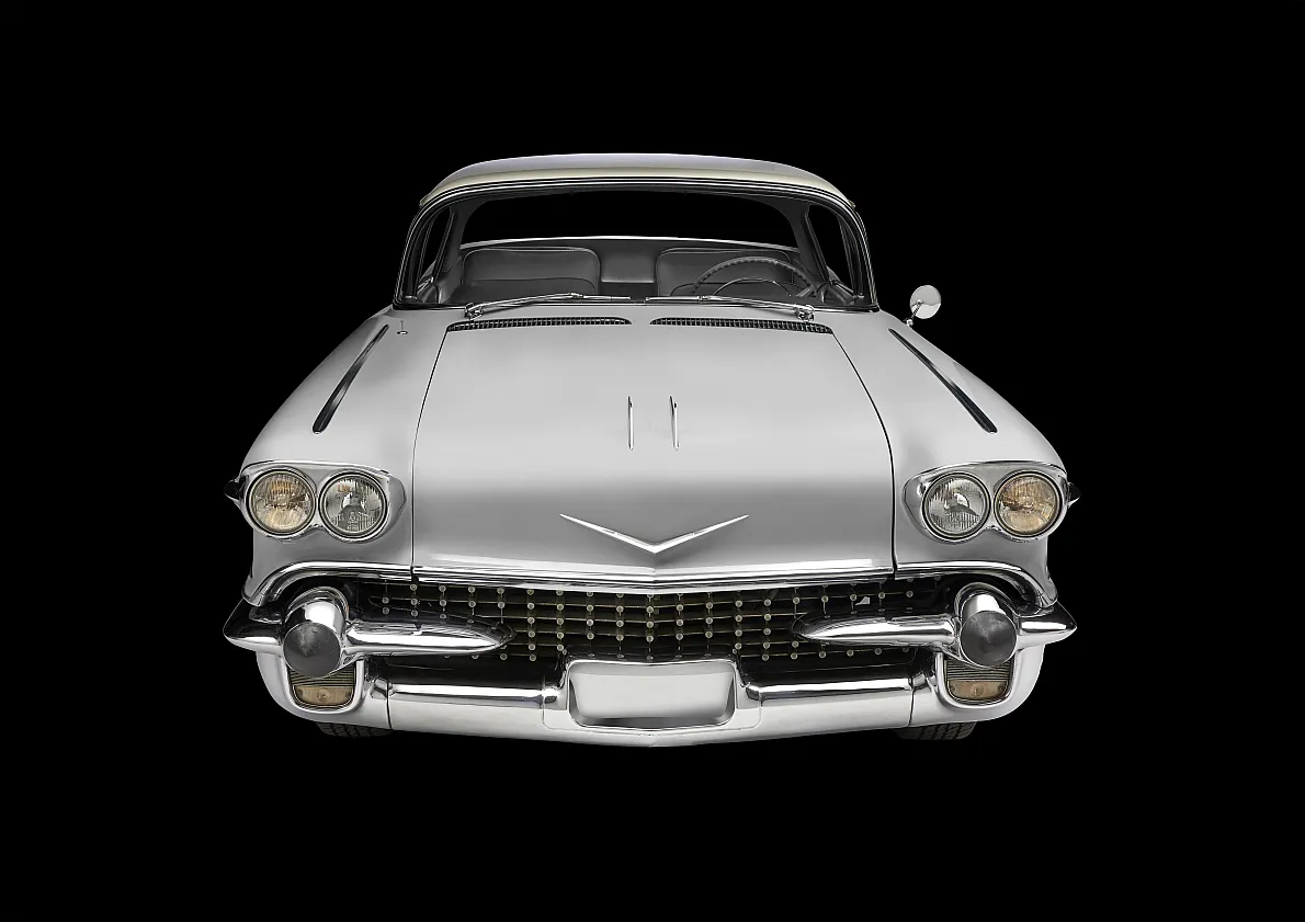 Frontansicht eines silbernen Oldtimers mit markantem Kühlergrill, runden Scheinwerfern, Chromdetails und V-förmigem Emblem auf der Motorhaube.