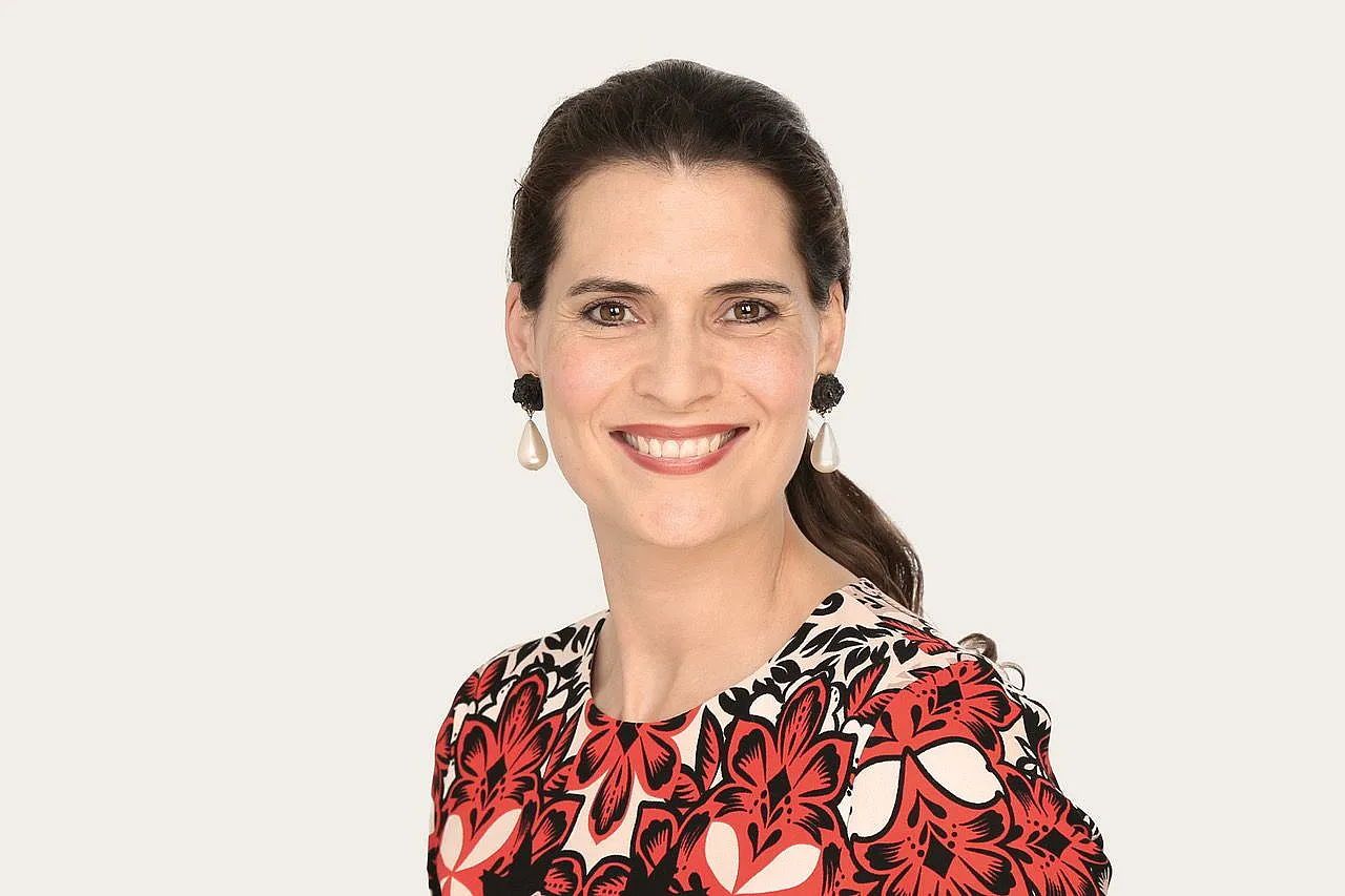 Janna Lena Baierle, eine Underwriter Art & Private Clients bei Hiscox, trägt ein Kleid mit rot-schwarzem Blumenmuster und große Perlenohrringe; das lange Haar ist nach hinten gebunden.