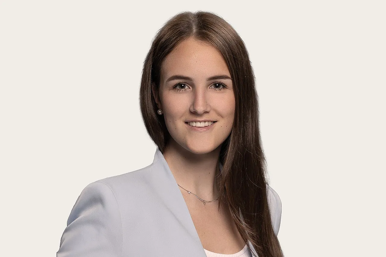 Ein Bild zeigt eine Person mit langen braunen Haaren, die einen hellen Blazer und ein weißes Oberteil trägt.