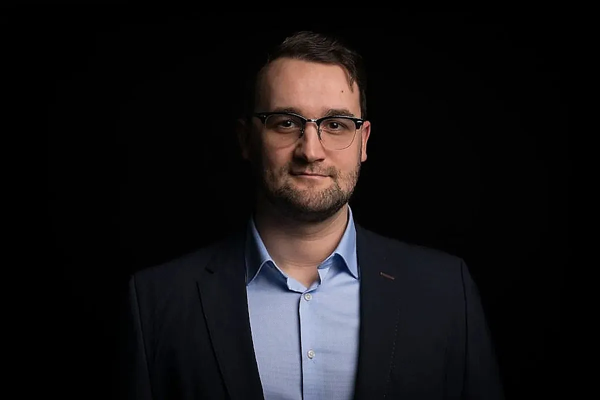 Klemens Lemke ist im Anzug und mit Brille vor einem dunklen Hintergrund. Er trägt einen marineblauen Blazer und ein hellblaues Hemd.