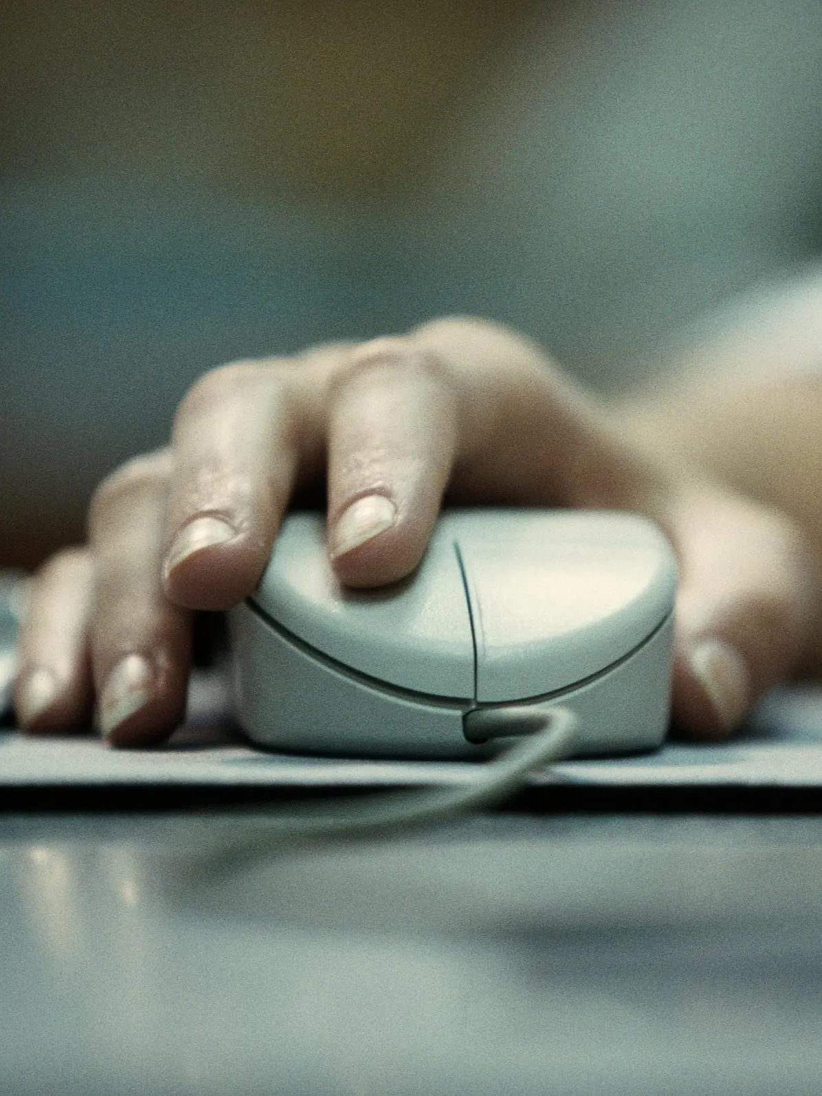 Eine Nahaufnahme einer Hand, die auf einer Computermaus ruht. Die Hand ist in Position, um die linke Maustaste zu klicken, und ein Kabel ist an der Vorderseite der Maus sichtbar. 