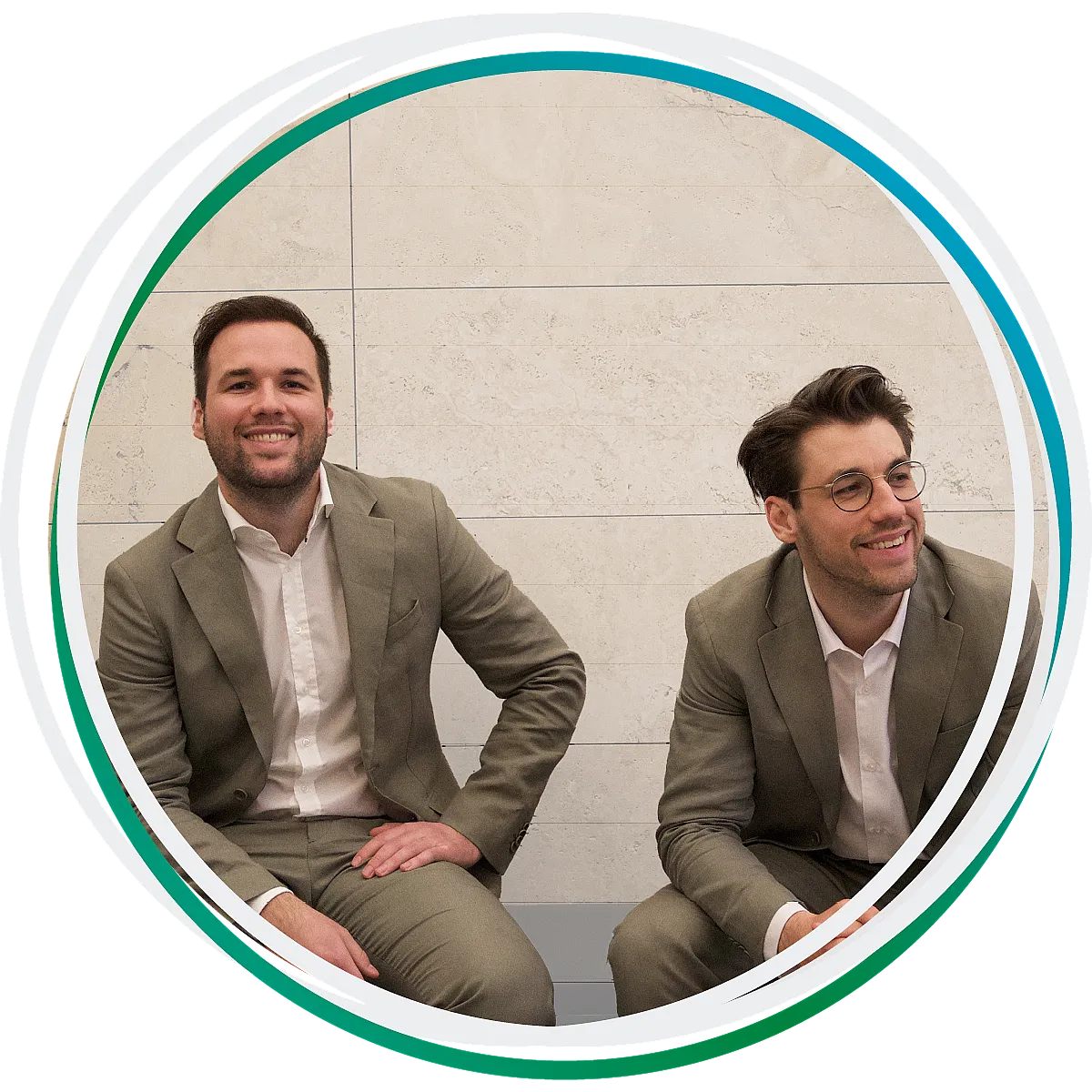 Die Rechtsanwälte Niklas und Lukas Hufeld sitzen vor einer Mauer und lächeln. Beide tragen einen beigen Anzug.