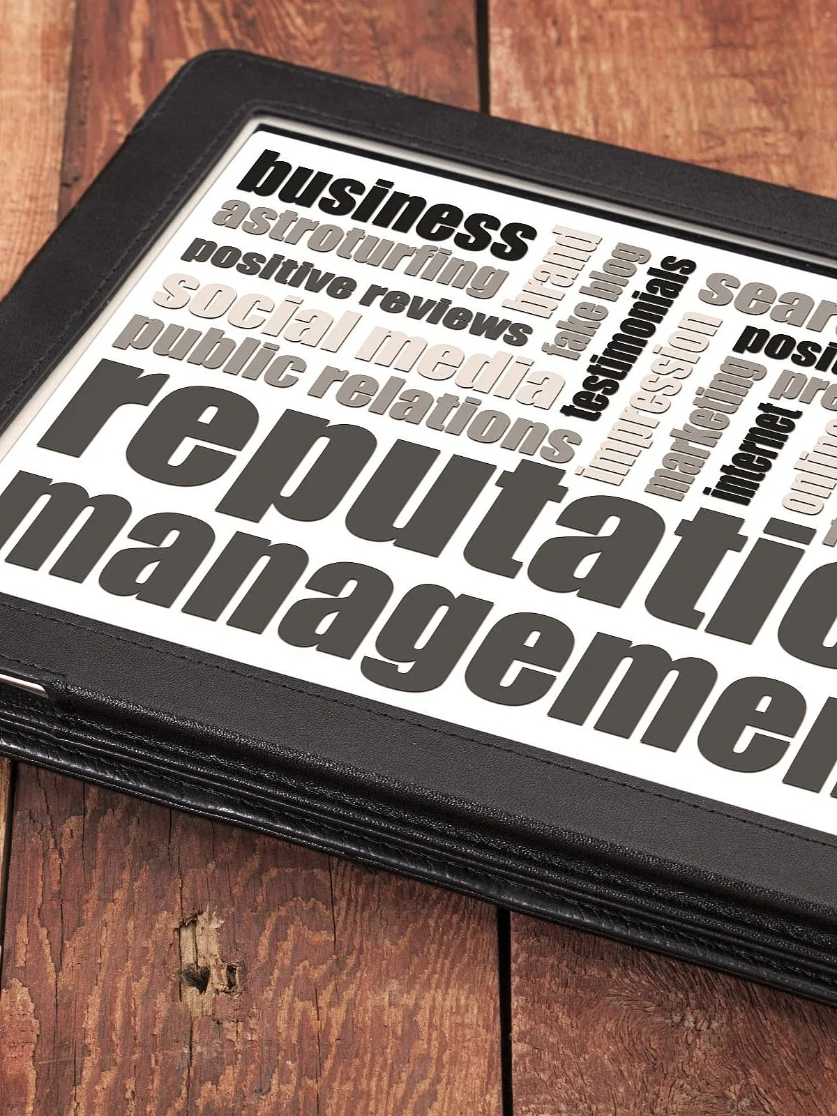 Tablet mit einer Wortwolke zum Thema "Reputation Management", auf einem rustikalen Holztisch liegend. Die Wörter umfassen Begriffe wie "business", "positive reviews", "public relations" und "ethics".